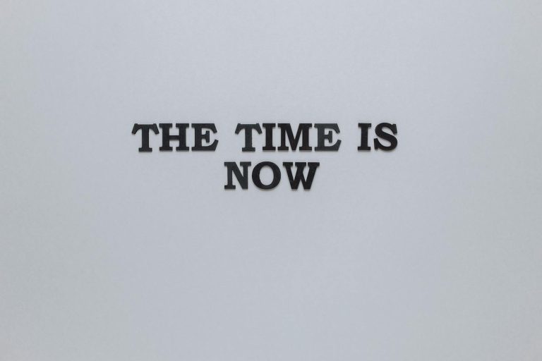 Minimalist poster with the motivational quote 'The Time is Now' on a gray background.